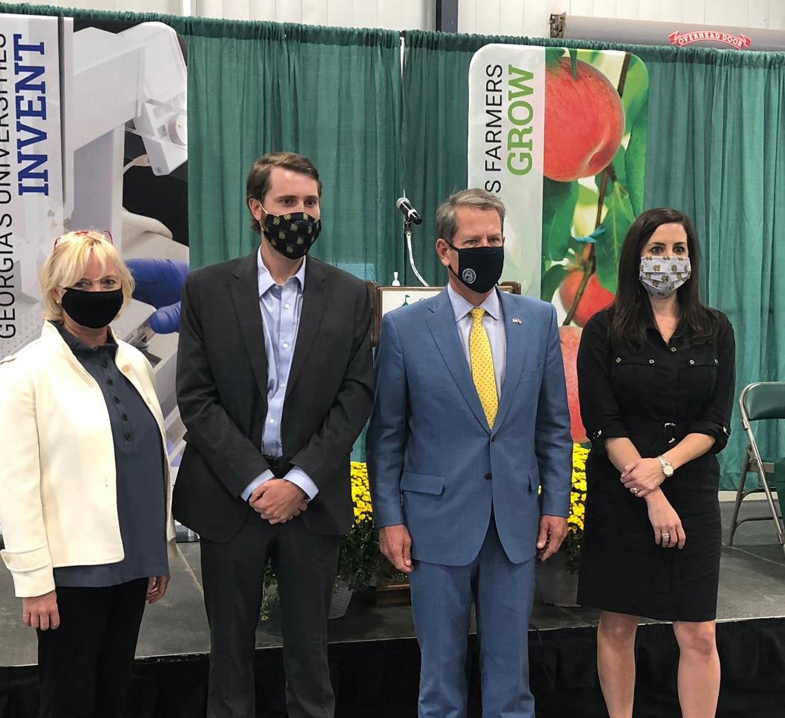 Four masked people standing in front of a Georgia's Universities Invent banner with Governor Brian Kemp