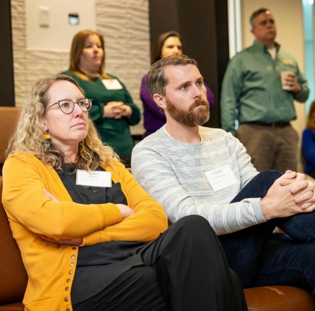 Chris Cornelison seated in an audience next to a colleague, both wearing name badges, at an industry event